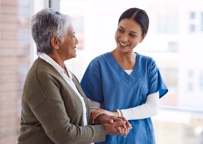 A caregiver with an elderly woman steadying herself on the caregivers arm