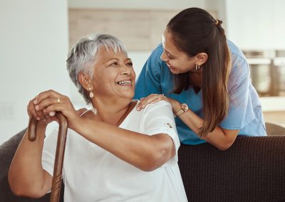 A caregiver with an elderly woman holding a cane and smiling