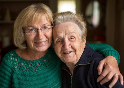 A caregiver with an elderly woman hugging and smiling