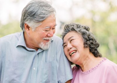 an elderly Asian couple both smiling on the sofa