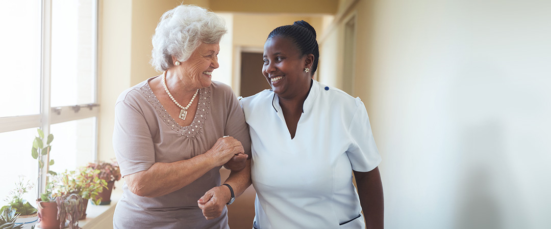 An African American nurse walking with a resident in the hallway