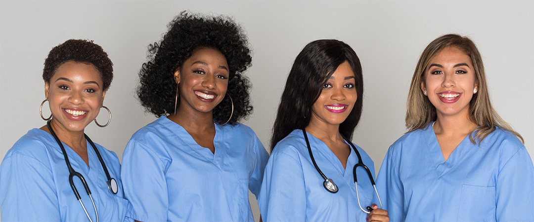 four female nurses in blue scrubs smiling