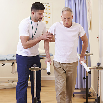 A rehab therapist helping an elderly gentleman to walk in the rehab gym